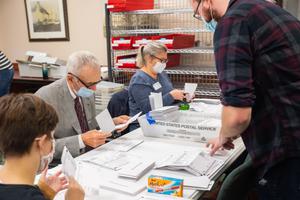 Volunteers open and sort mail-in ballots in Erie while poll watchers observe.