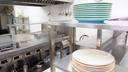 A stock image of plates stacked on a stainless steel shelf in a kitchen. A stock image of plates stacked on a stainless steel shelf in a kitchen.