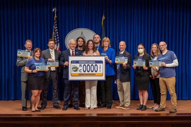 Attendees pose at a 2024 Harrisburg event celebrating a license plate featuring the state amphibian.