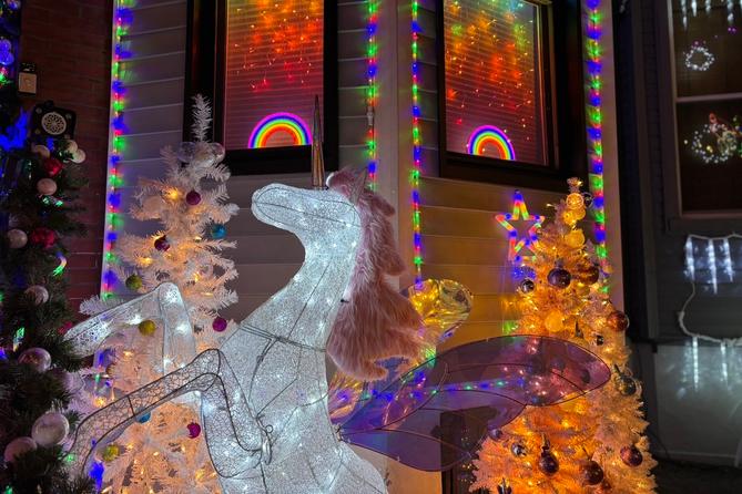 A unicorn figure and artificial Christmas trees in front of a house with rainbow-lit windows.