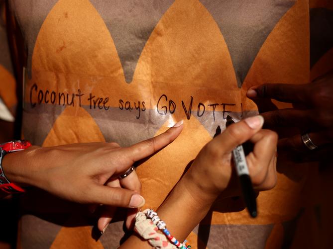 Devisha Bisaria, campus organizer for Project 26, writes “Coconut tree says go vote” on the coconut tree outfit of University of Pittsburgh student Kamal Miya on the campus of the University of Pittsburgh on Nov. 5., 2024.